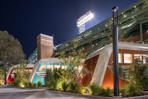 A modern building with a glass facade, a covered walkway, and a large illuminated structure in the background.