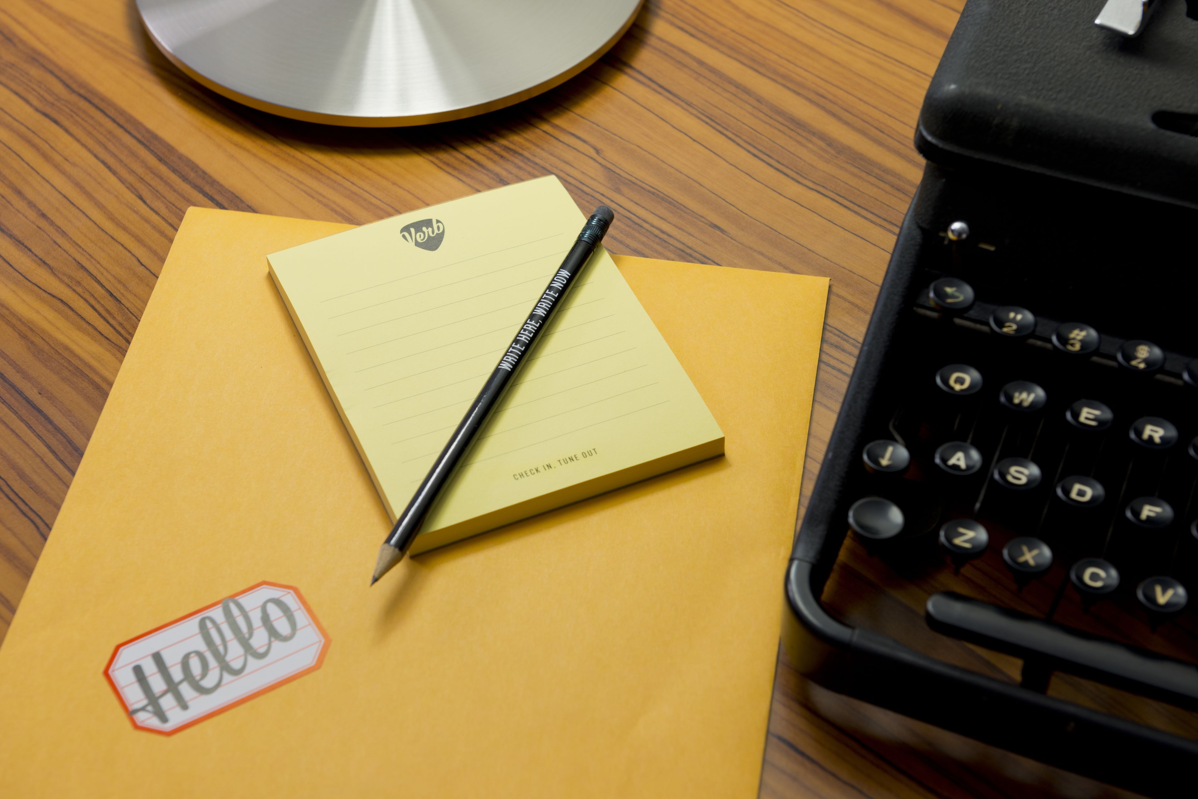 A desk with a typewriter, a yellow notepad, a pen, and a sticky note with "Hello" written on it.