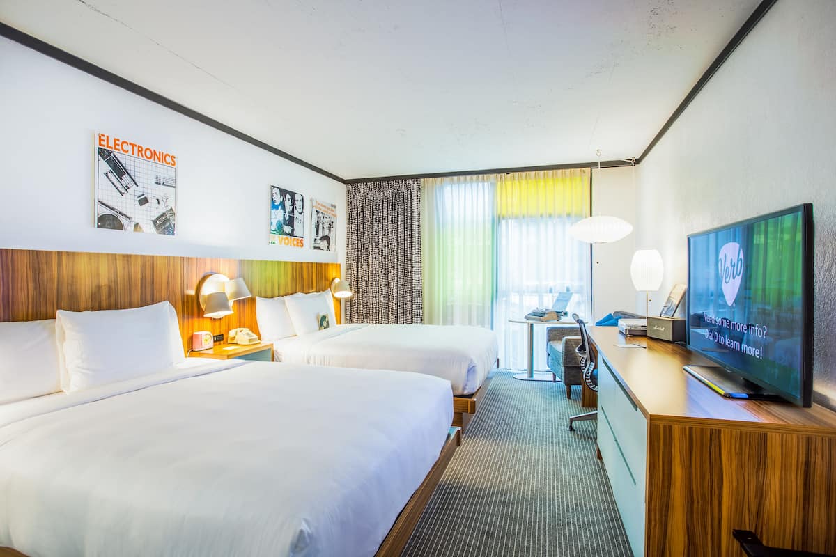A hotel room with two beds, a desk with a television, and a small table with a lamp.
