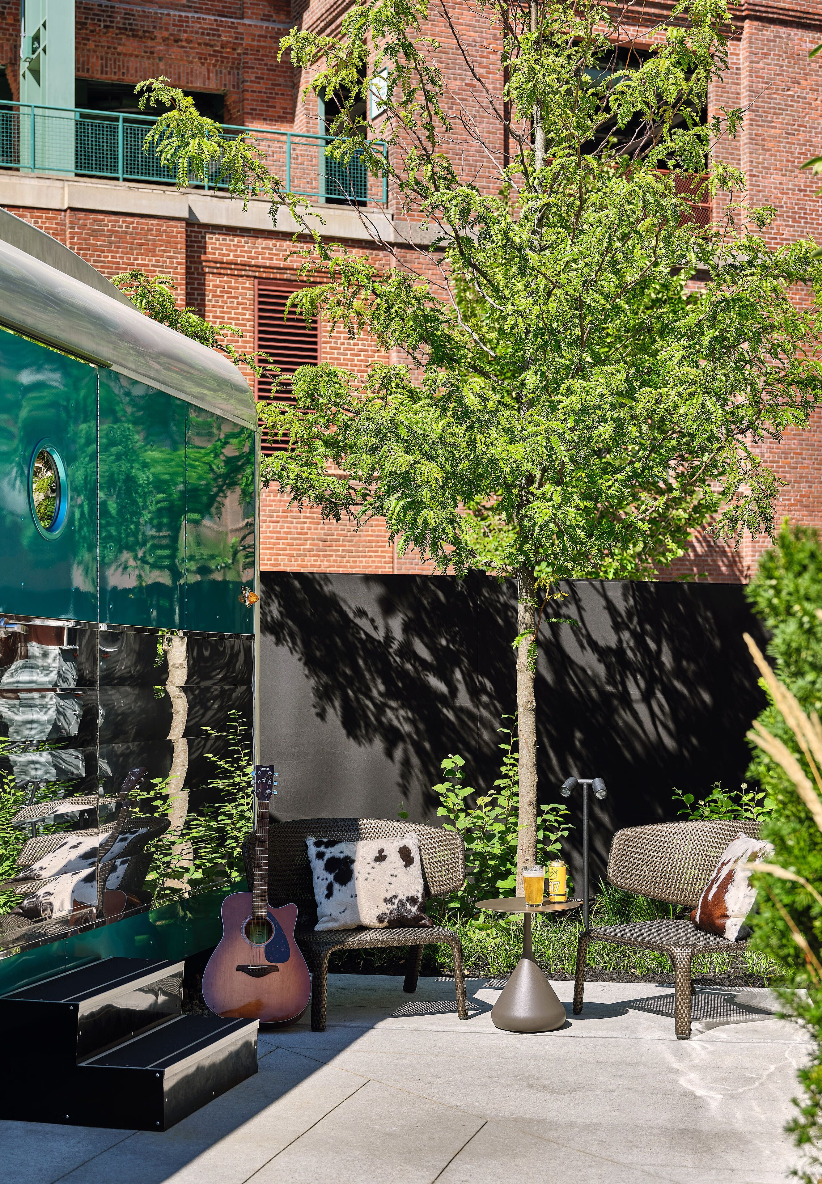 An outdoor seating area with a guitar, a table with drinks, and a tree.