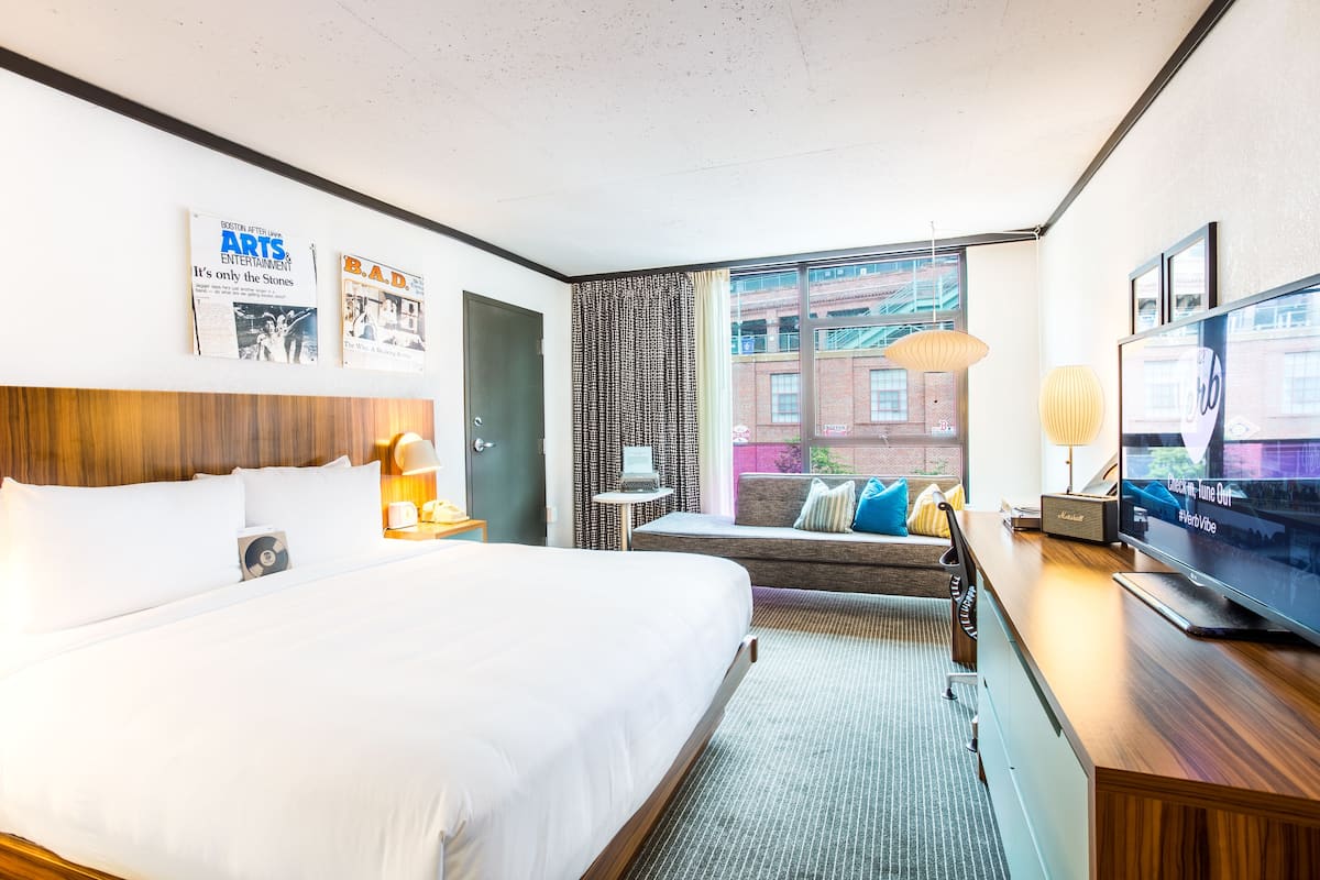 A hotel room with a large bed, a sofa, a television, and a window with a view of buildings.