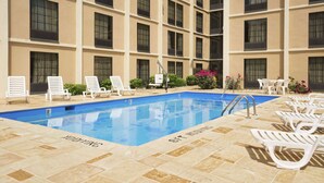 Una piscina con sillas de descanso y un edificio con varias ventanas al fondo.