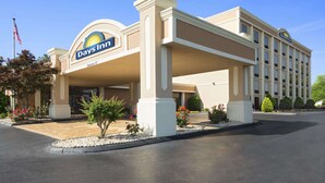 Un hotel Days Inn con entrada despejada, estacionamiento y un área ajardinada con árboles pequeños y flores.