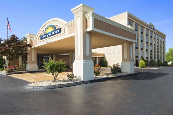 A Days Inn hotel with a clear entrance, a parking lot, and a landscaped area with small trees and flowers.
