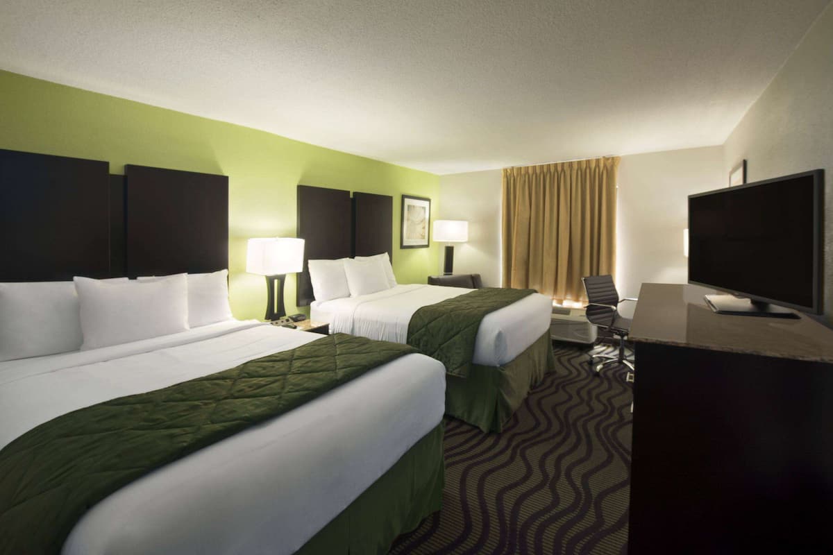 A hotel room with two beds, a desk, a television, and a window with curtains.