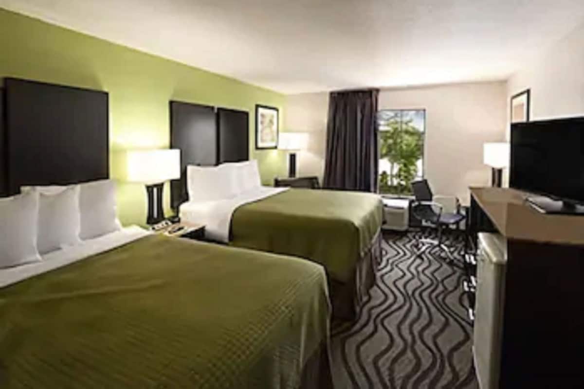 A hotel room with two beds, a desk, a chair, a television, and a window.