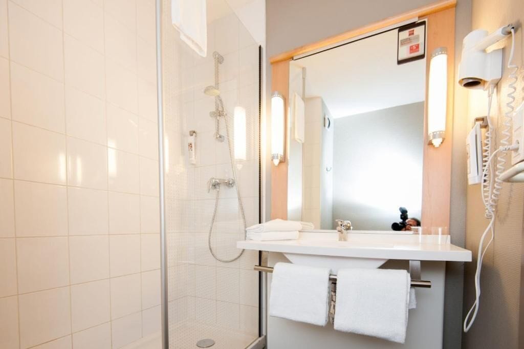 A modern bathroom with a glass shower enclosure, a white sink with a mirror, and a hairdryer mounted on the wall.