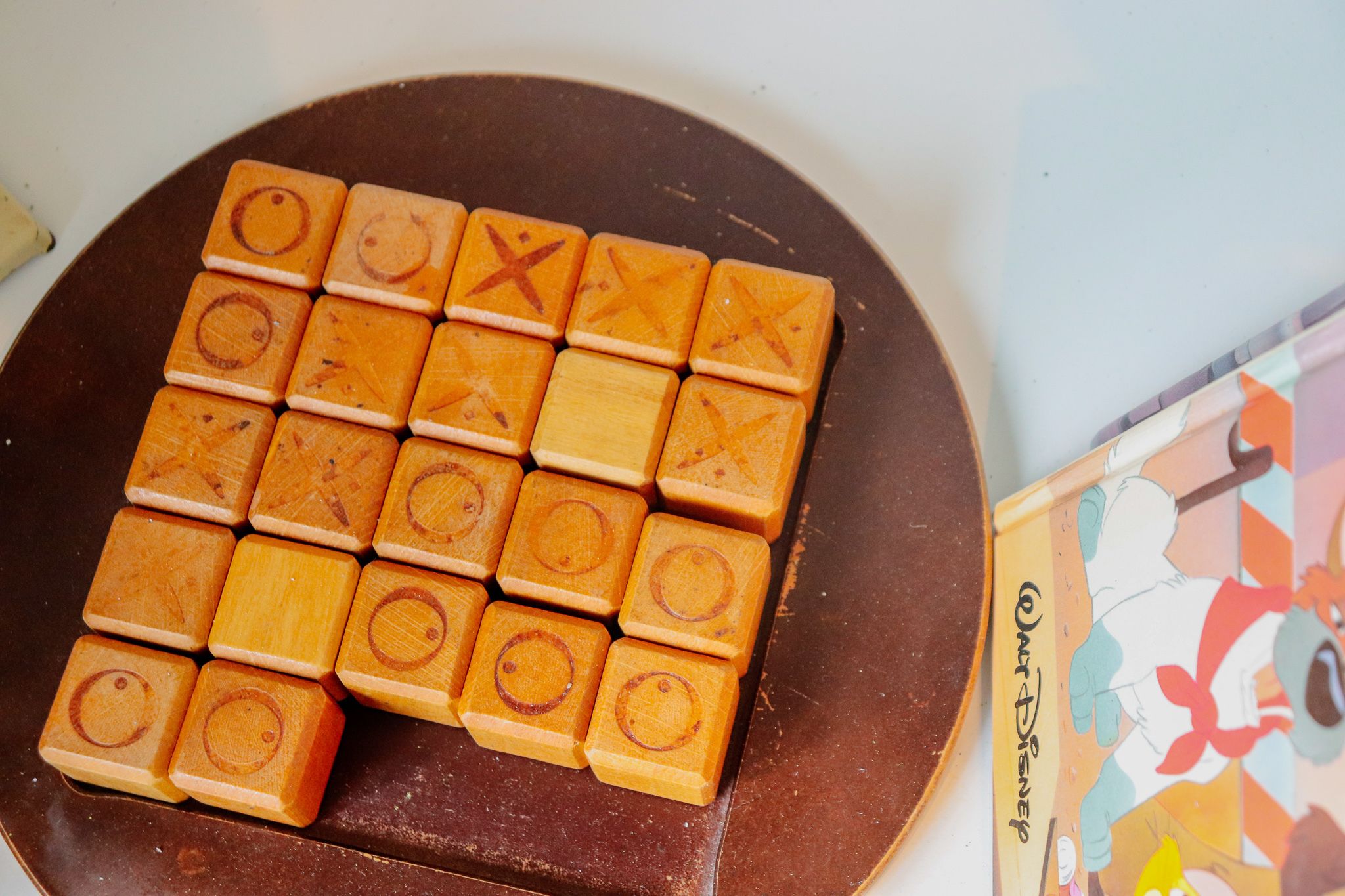 Een houten spel met pionnen voorzien van symbolen, geplaatst op een bruin oppervlak naast een kleurrijk kaartspel met Disney-thema.