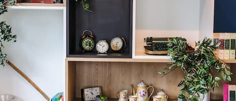 A bookshelf with books, clocks, a typewriter, and a teapot set.