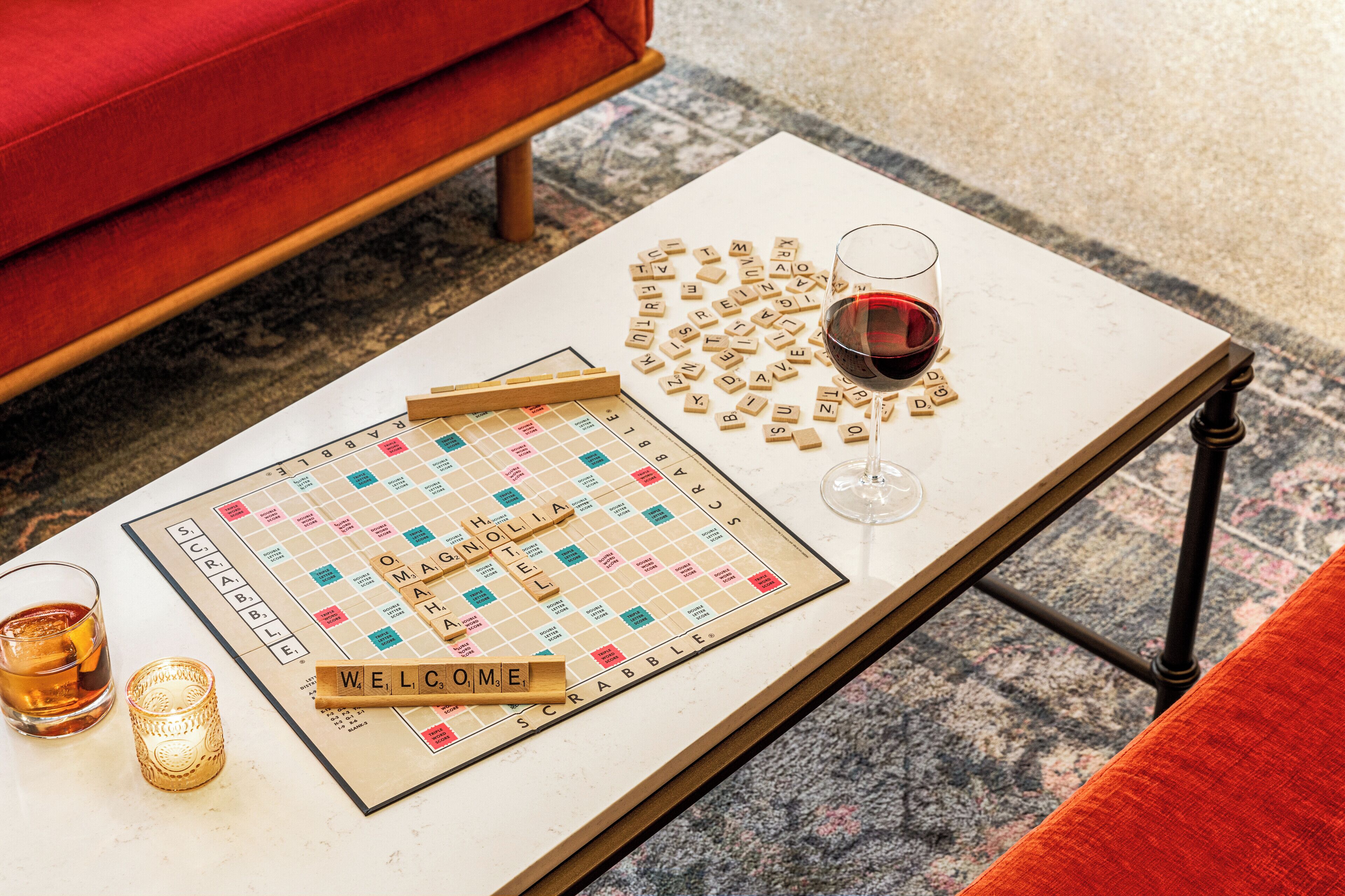 A Scrabble board with tiles and a glass of red wine on a white table.