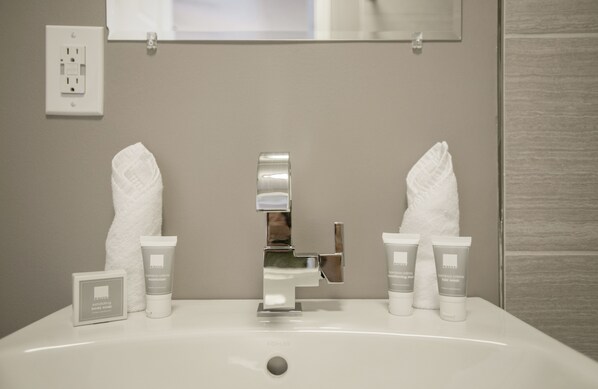 A bathroom sink with two white towels, two tubes of body cream, and a soap dispenser.
