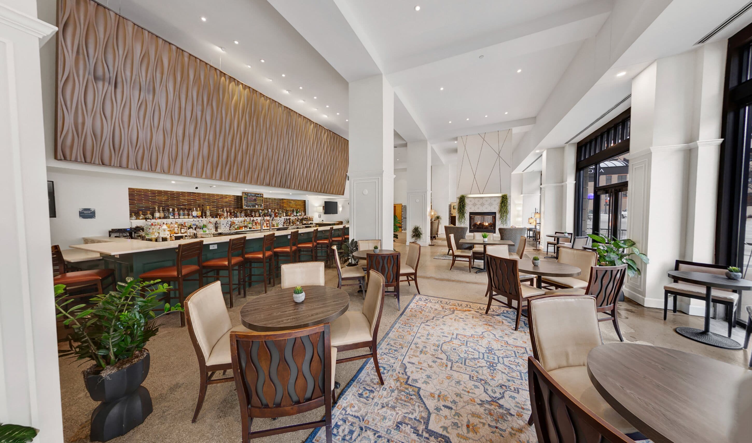 A spacious hotel lobby with a bar area, seating arrangements, and a decorative wall.