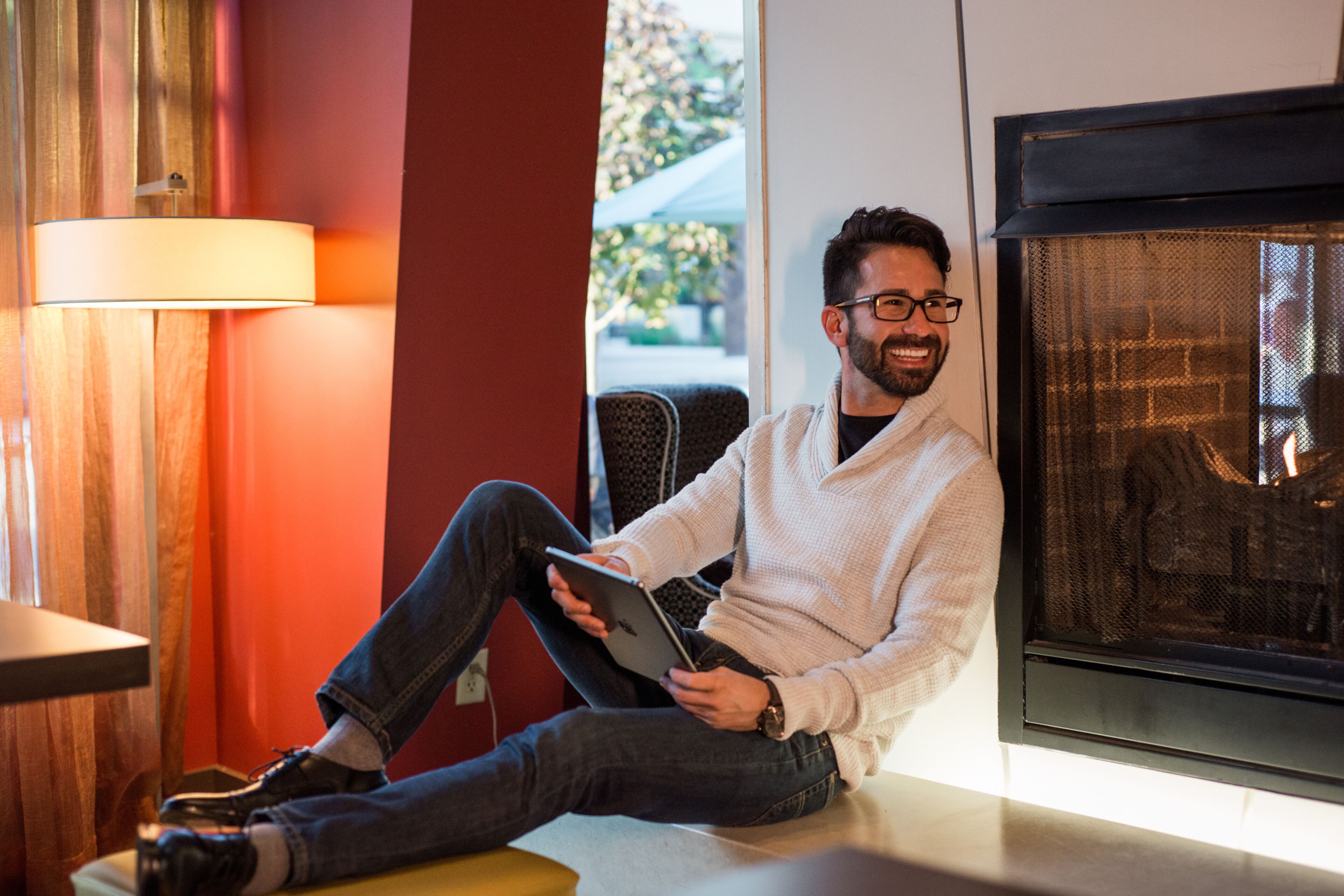 Une personne assise sur un banc dans une pièce avec une cheminée, tenant une tablette.