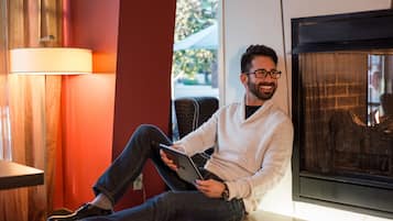 Une personne assise sur un banc dans une pièce avec une cheminée, tenant une tablette.