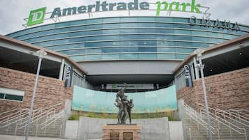 The exterior of Ameritrade Park with a large glass facade, a statue in front, and a sign above the entrance.