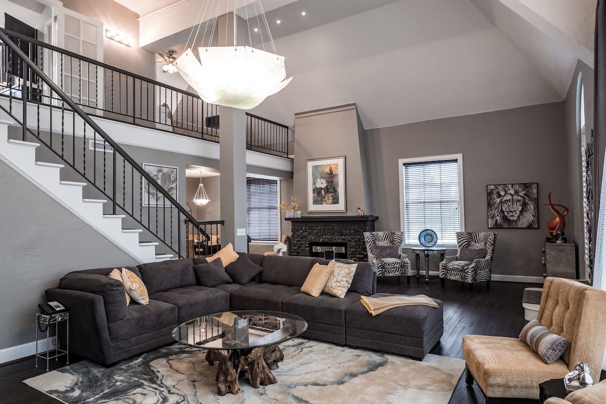 A spacious living room with a dark gray sectional sofa, a glass coffee table, and a staircase leading to an upper level.
