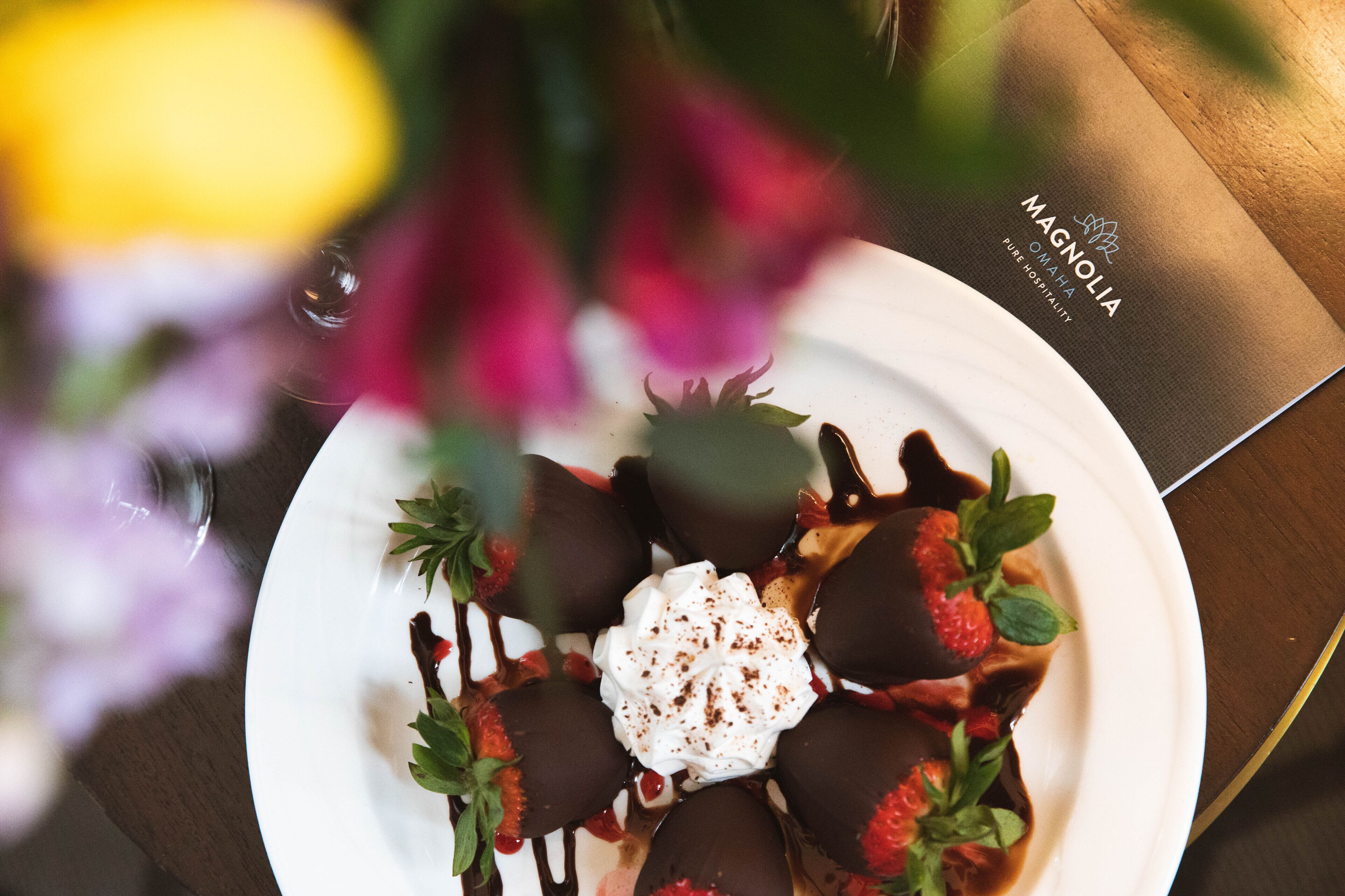 Un plato de postre con fresas bañadas en chocolate, crema batida y salsa de chocolate sobre un plato blanco.