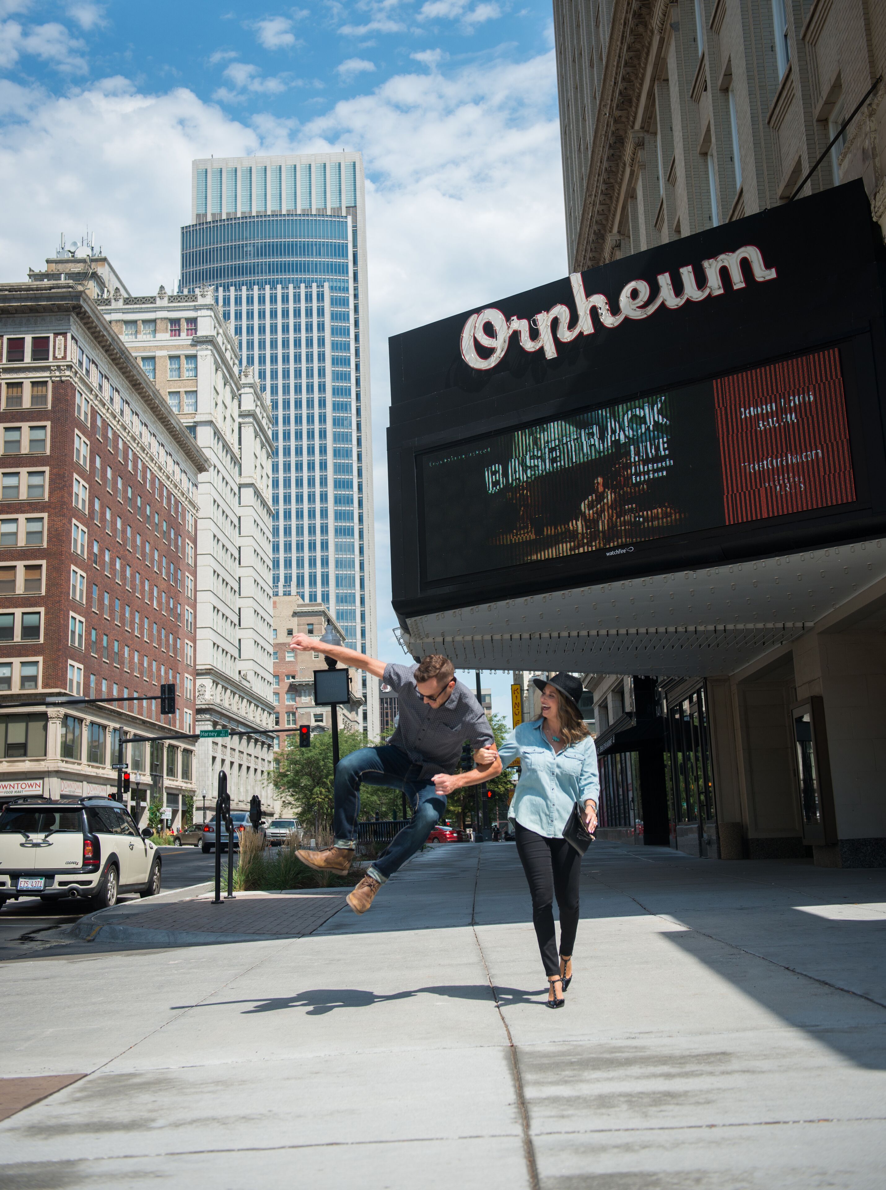 A city street with a large digital billboard advertising a theater.