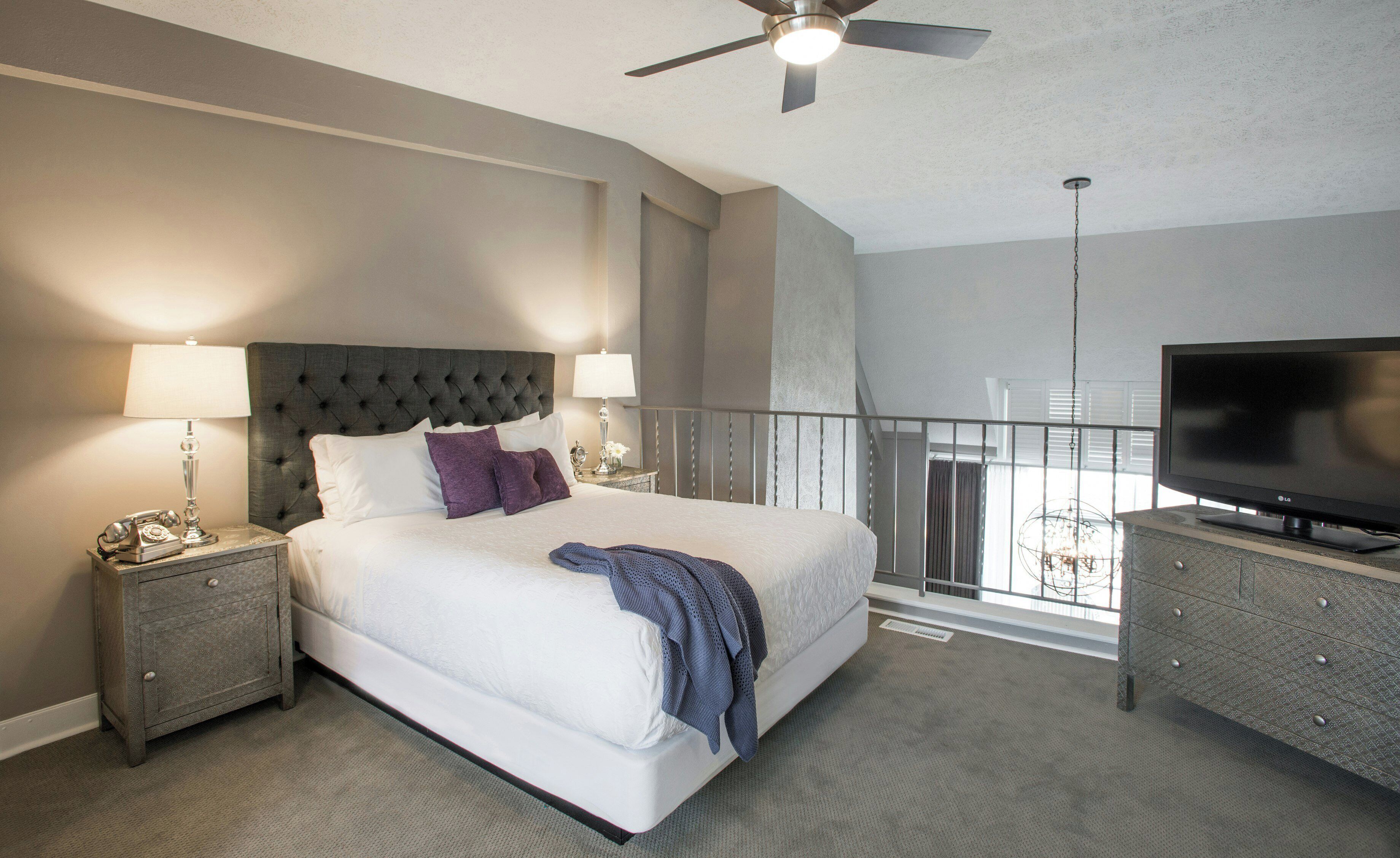 A hotel room with a bed, a television, a nightstand, and a ceiling fan.