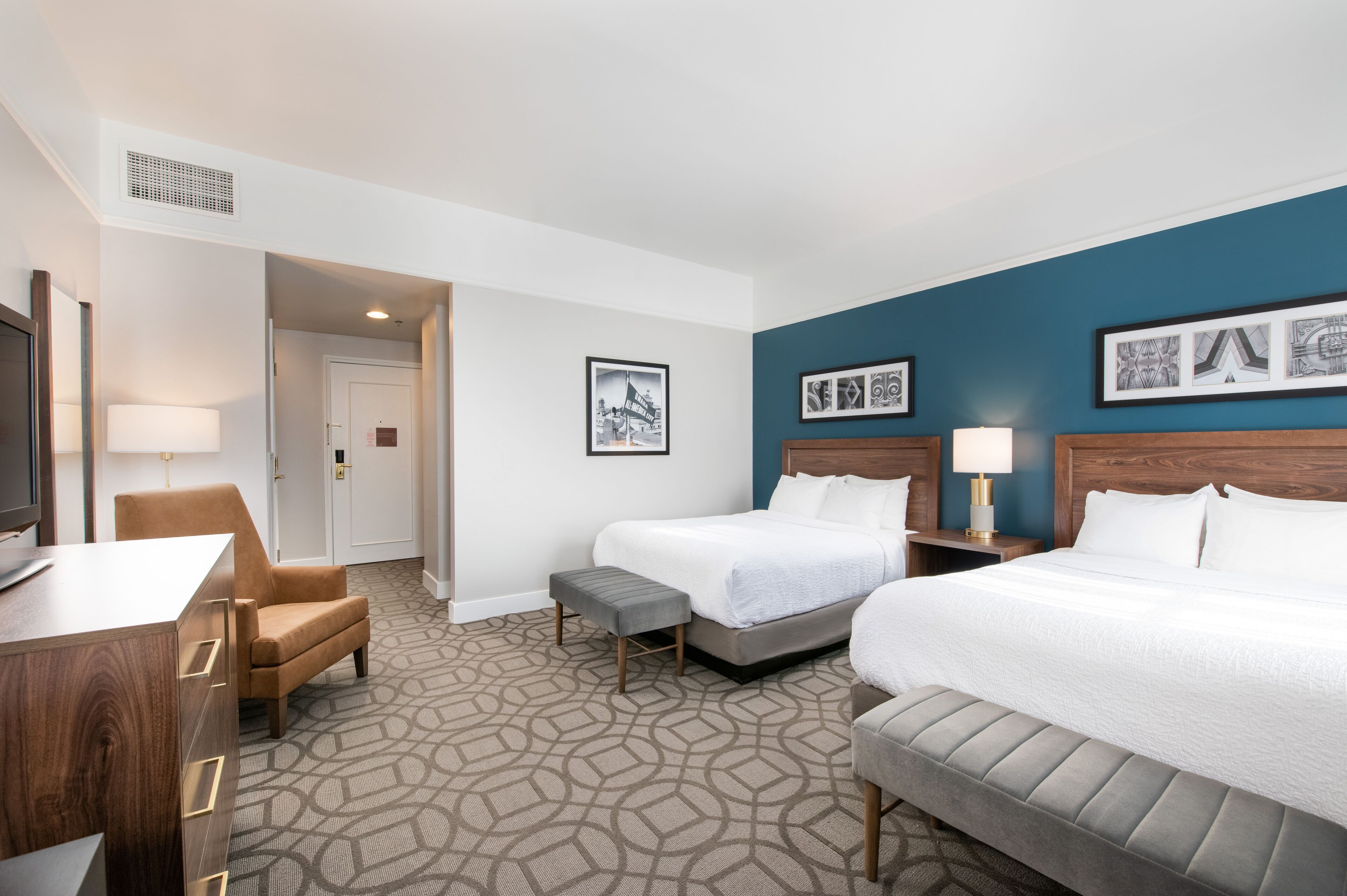 A hotel room with two beds, a desk, a chair, and a television.