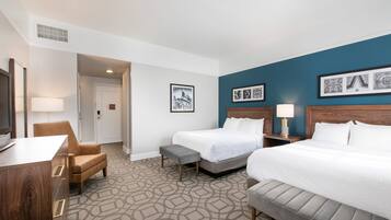 A hotel room with two beds, a desk, a chair, and a television.