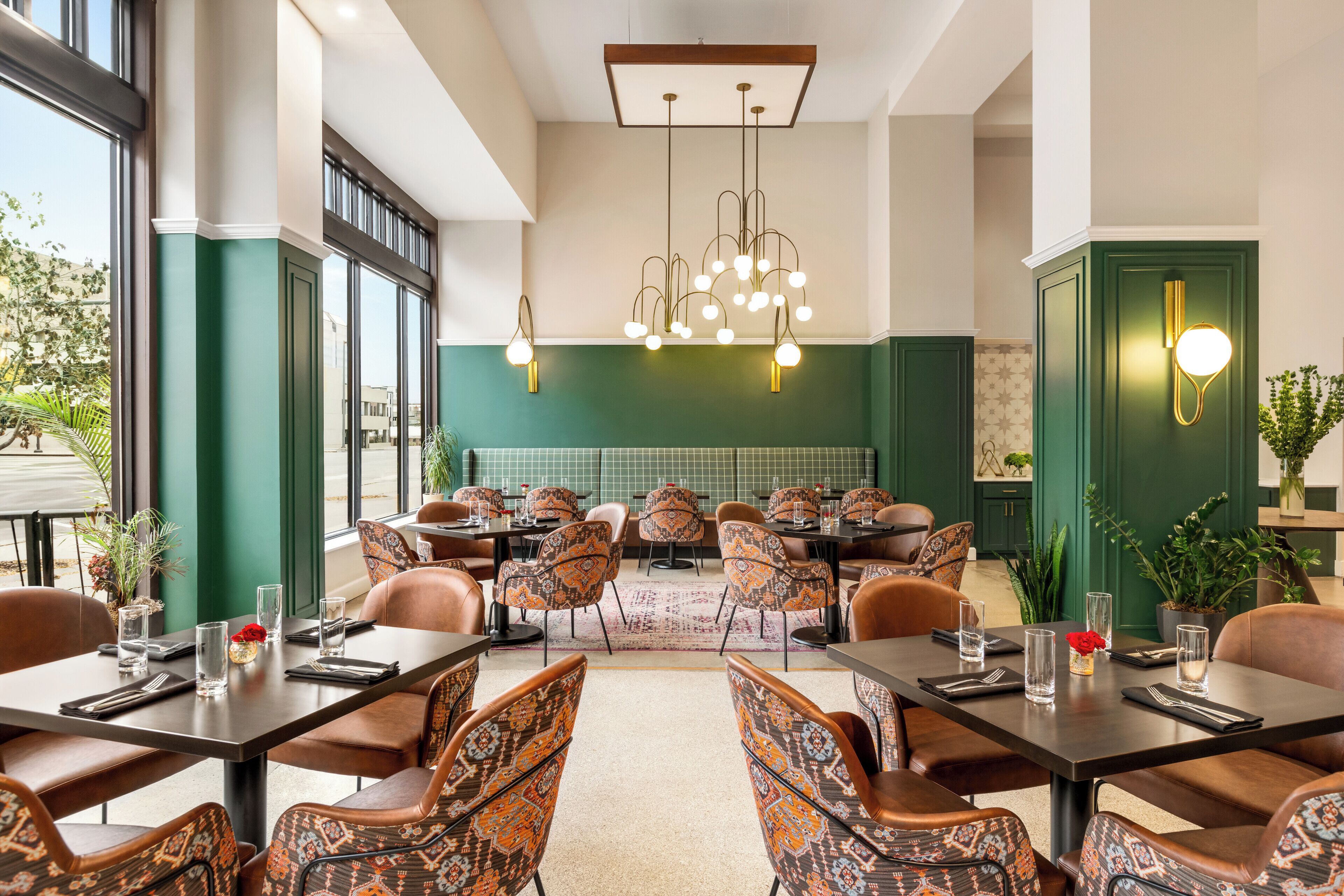 Un espace repas avec des tables et des chaises, un lustre et une vue sur l’extérieur.