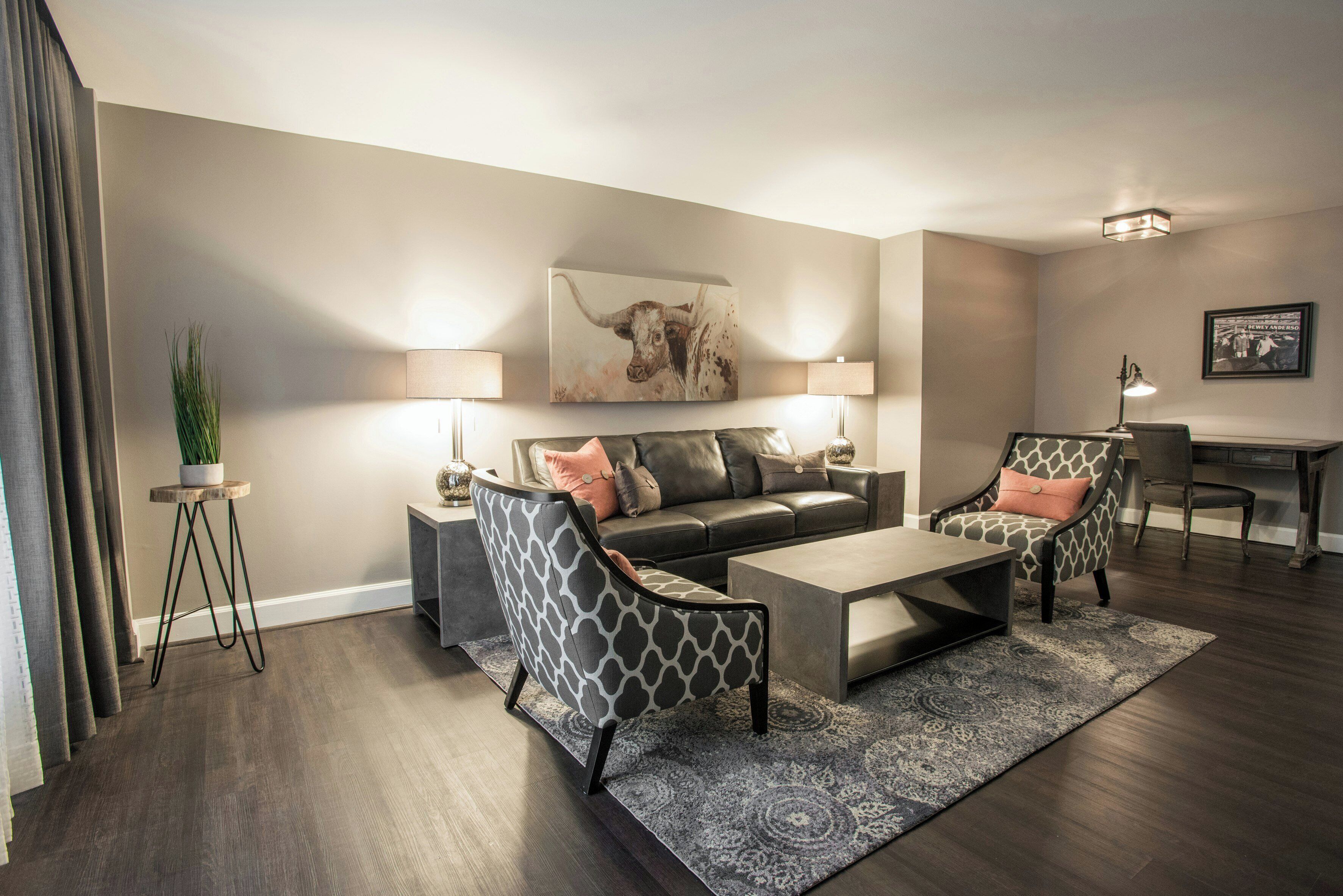 Een moderne woonkamer met een bank, twee fauteuils, een salontafel en een vloerkleed. Aan de muur hangt een schilderij en op een bijzettafeltje staat een lamp.