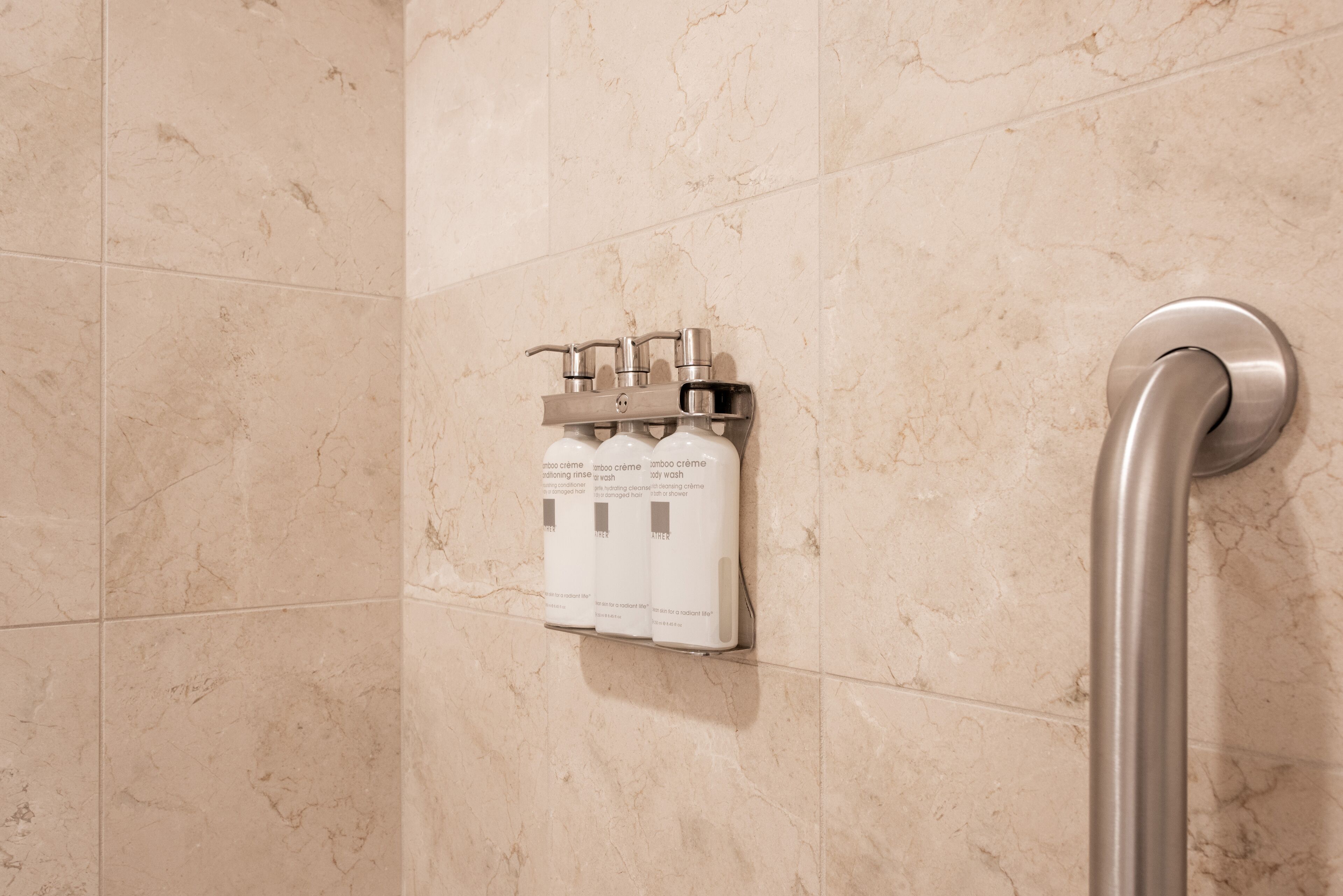 A bathroom with a handrail, a wall-mounted soap dispenser, and a showerhead.