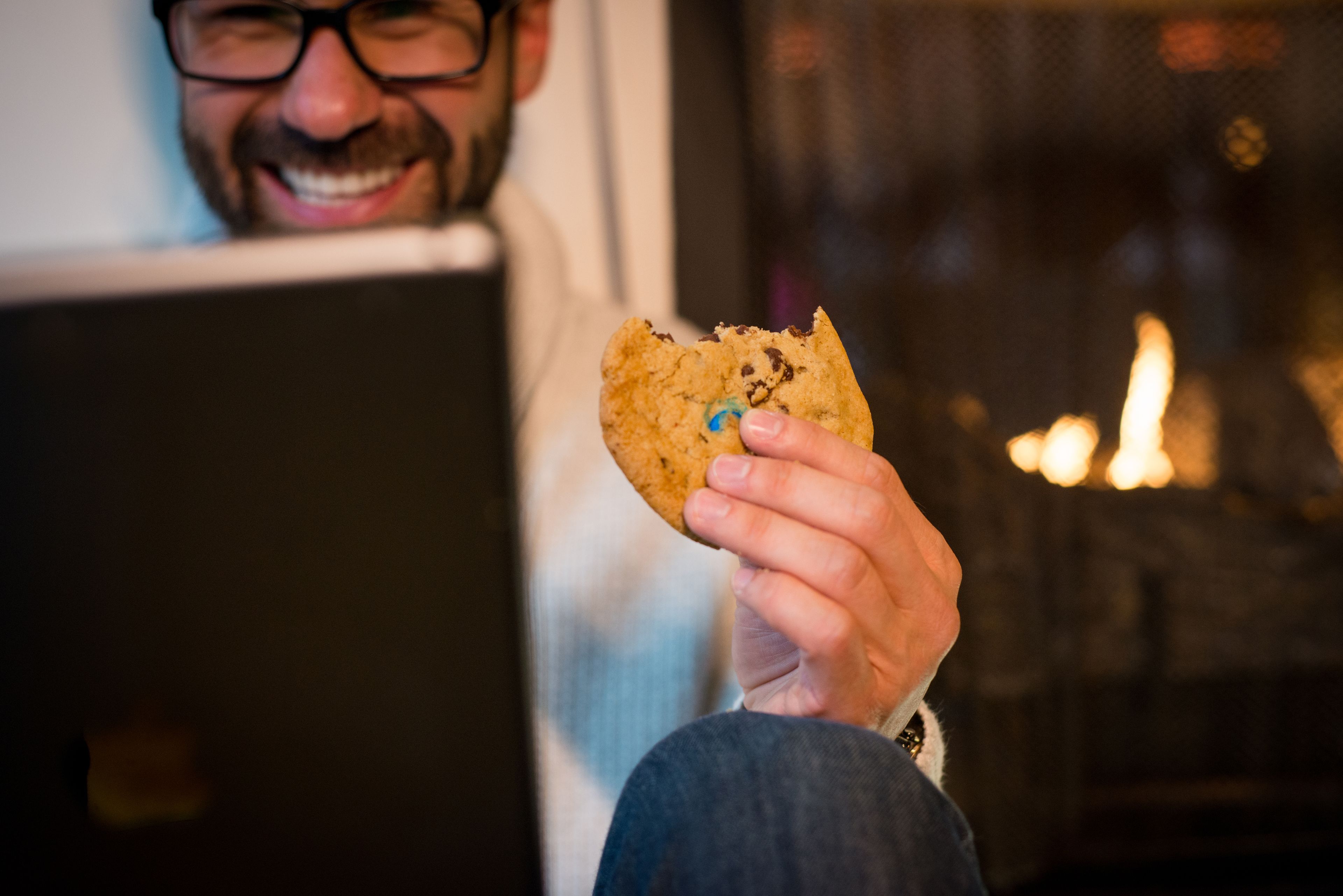 Une personne tenant un biscuit aux pépites de chocolat, assise devant un ordinateur portable.