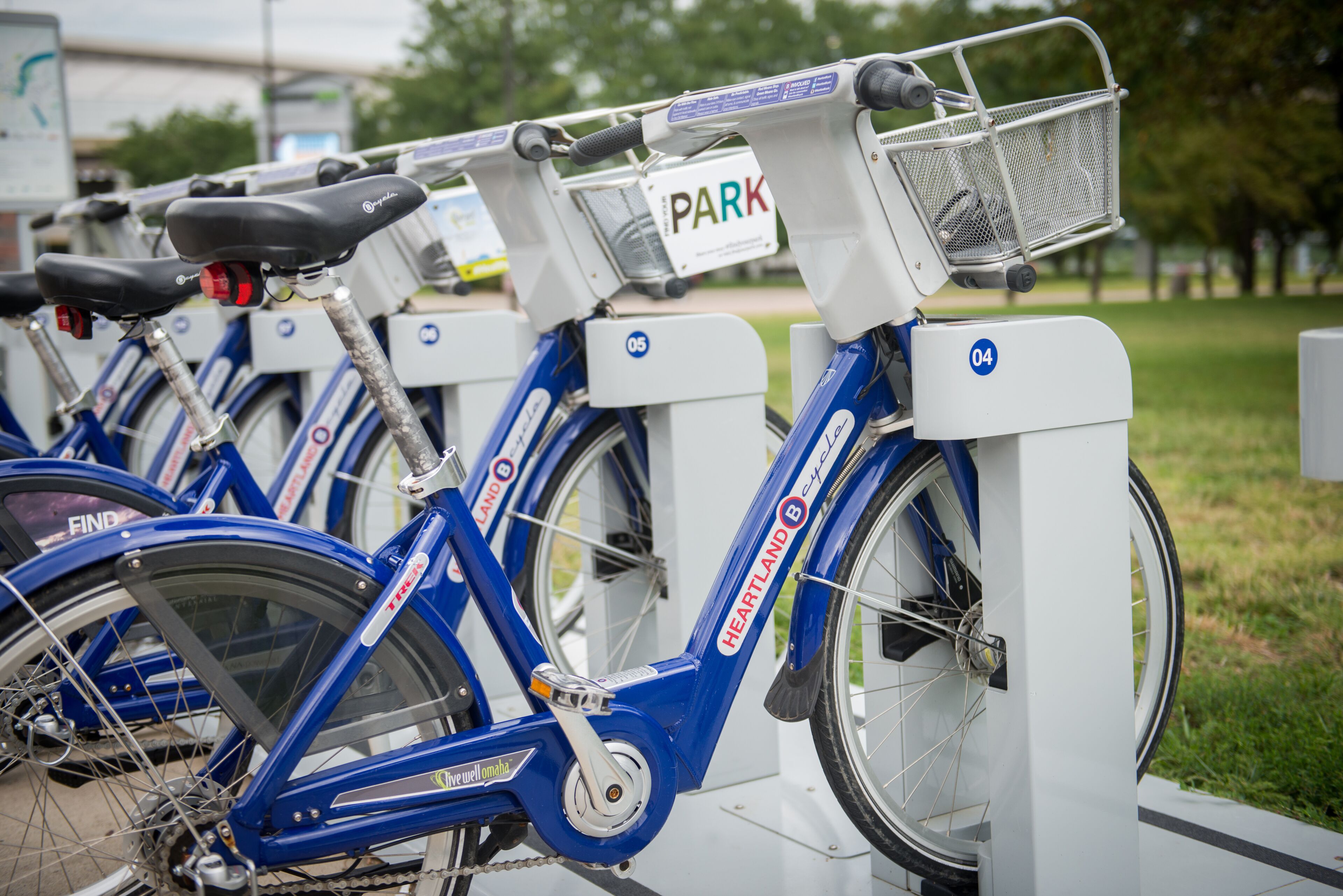 A row of blue bicycles with a white frame, each equipped with a basket and a sign that reads "PARK".