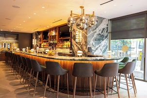 A modern bar area with a marble countertop, multiple bar stools, and a large screen.