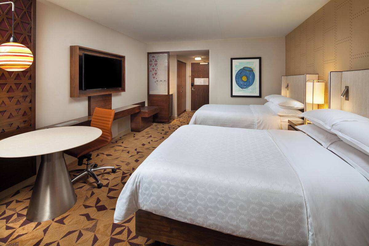 A hotel room with two beds, a TV, a desk, and a chair.