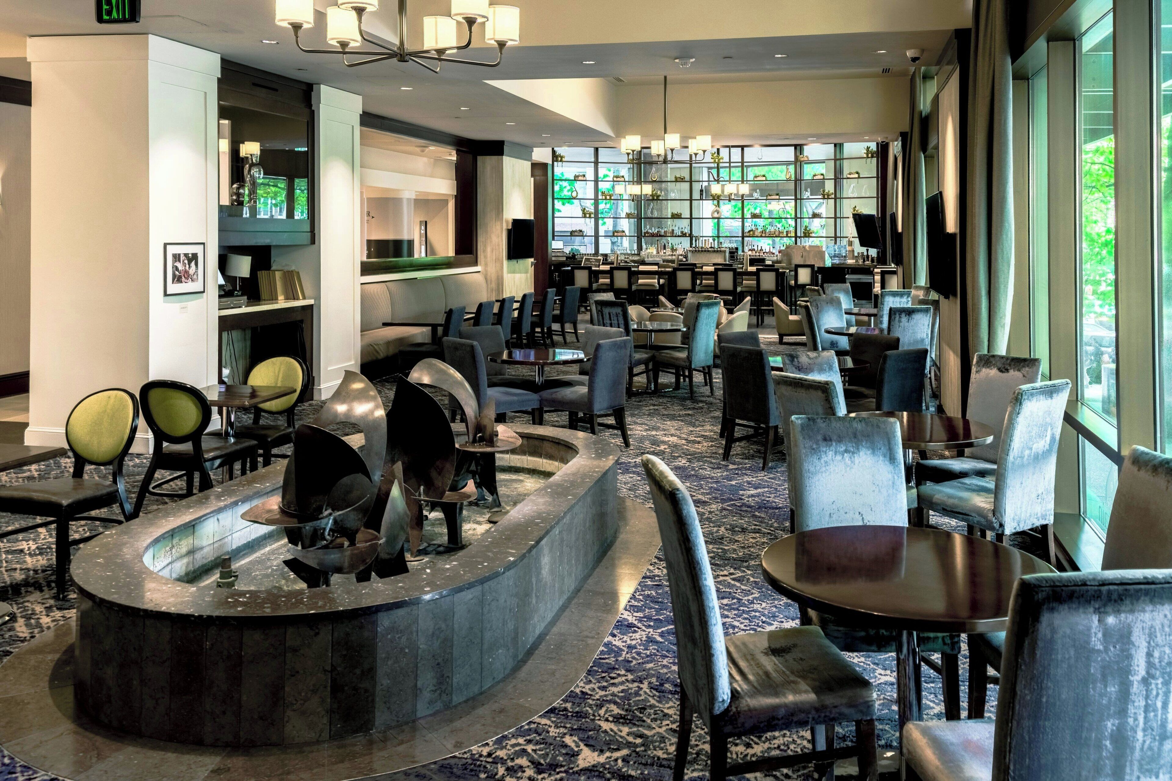 A hotel lobby with a reception desk, seating area, and large windows offering a view of greenery outside.