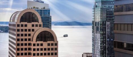 Un edificio moderno de gran altura con fachada curva y un amplio ventanal arqueado, con vistas a una masa de agua donde se divisa un barco a lo lejos.