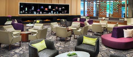 A spacious lobby with multiple seating areas, a large flat-screen TV, and a decorative wall with geometric patterns.