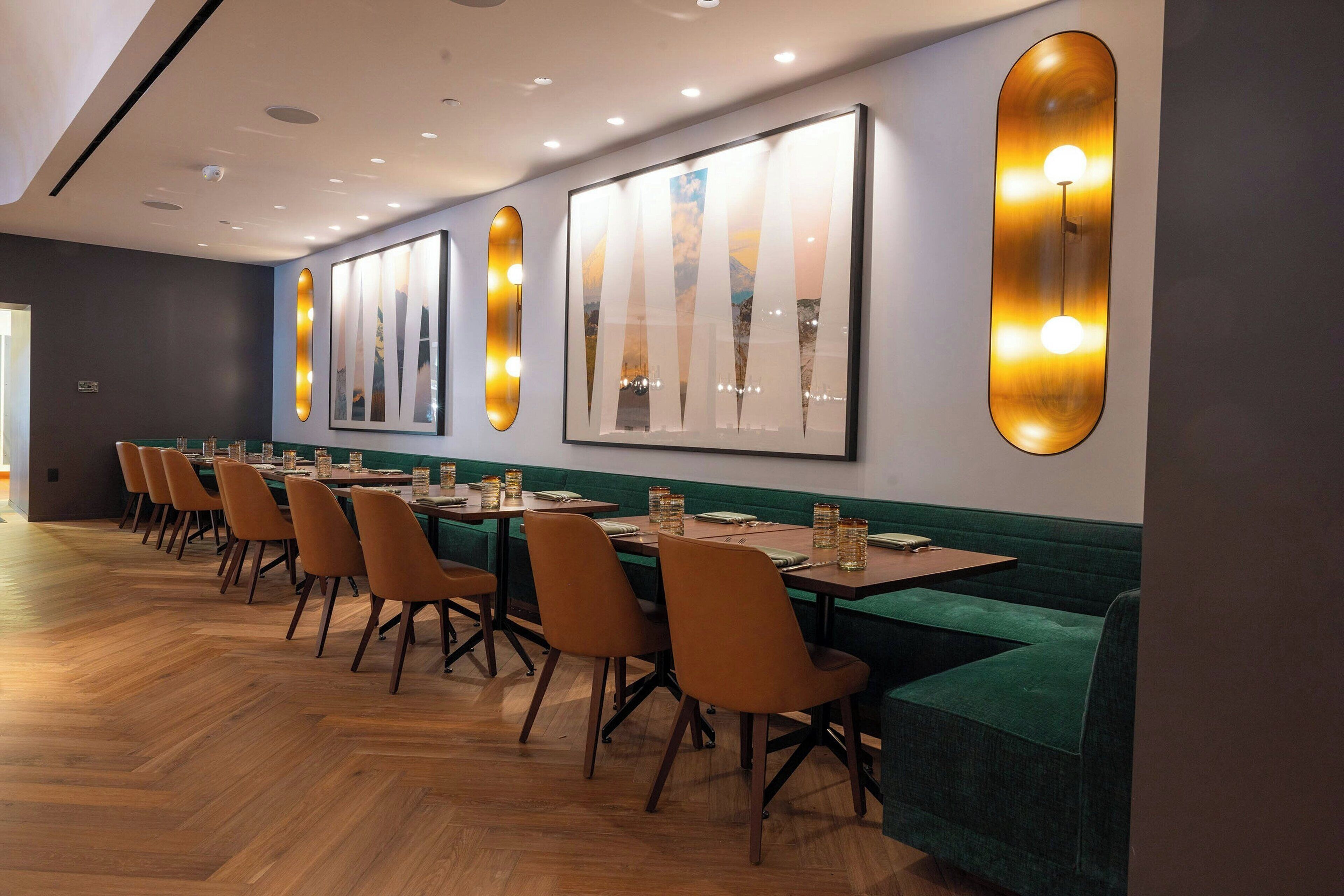 A restaurant with long wooden tables, orange chairs, and green cushioned seating.