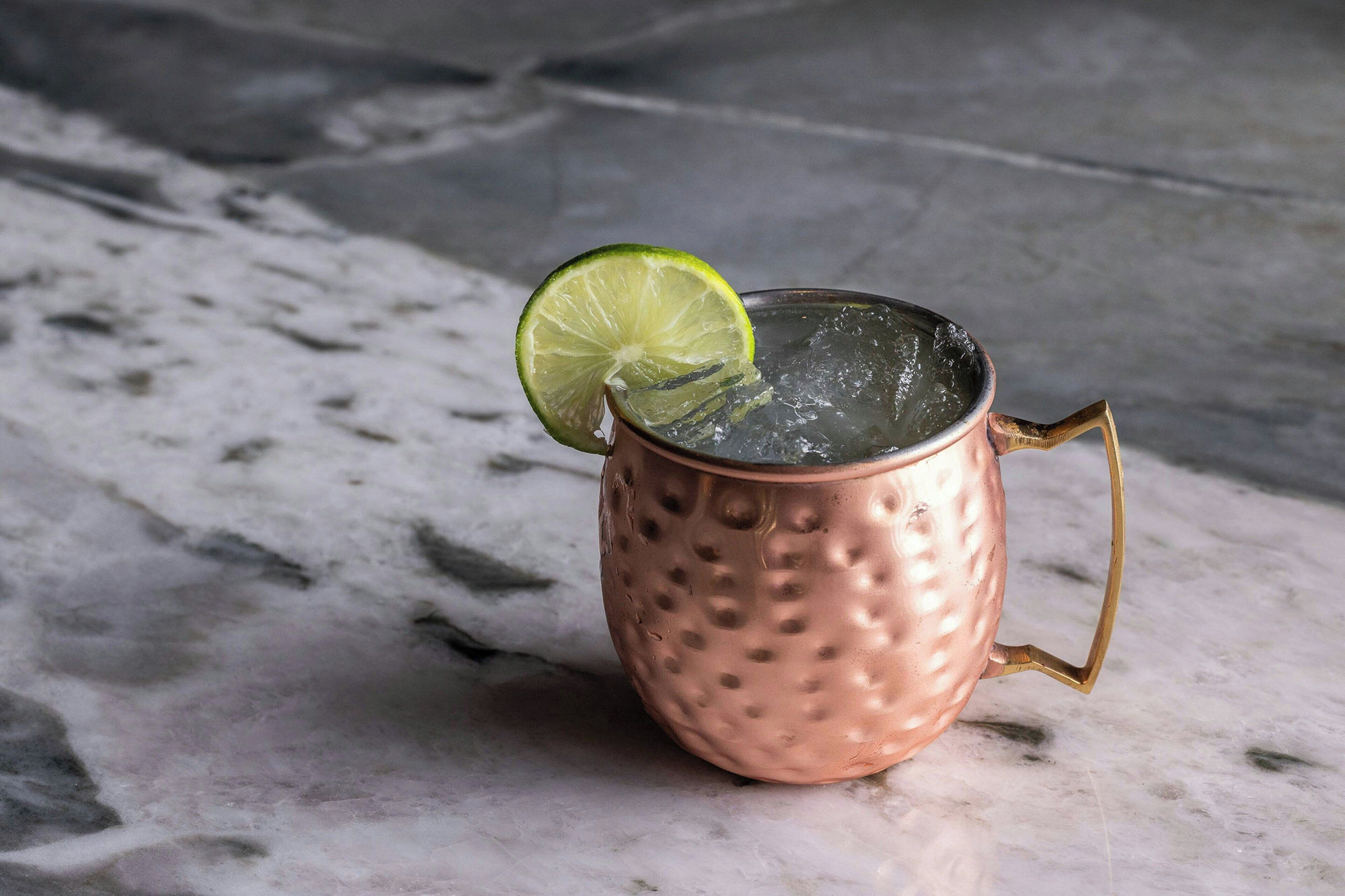 A copper mug with a handle, filled with ice and a lime slice on top, placed on a marble surface.