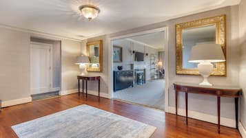 A spacious hallway with hardwood floors, a blue striped rug, and two ornate tables with lamps.