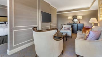 Ein Hotelzimmer mit einem großen Flachbildfernseher, einem Sofa, einem Sessel, einem kleinen Tisch und einer Kommode mit Lampen.