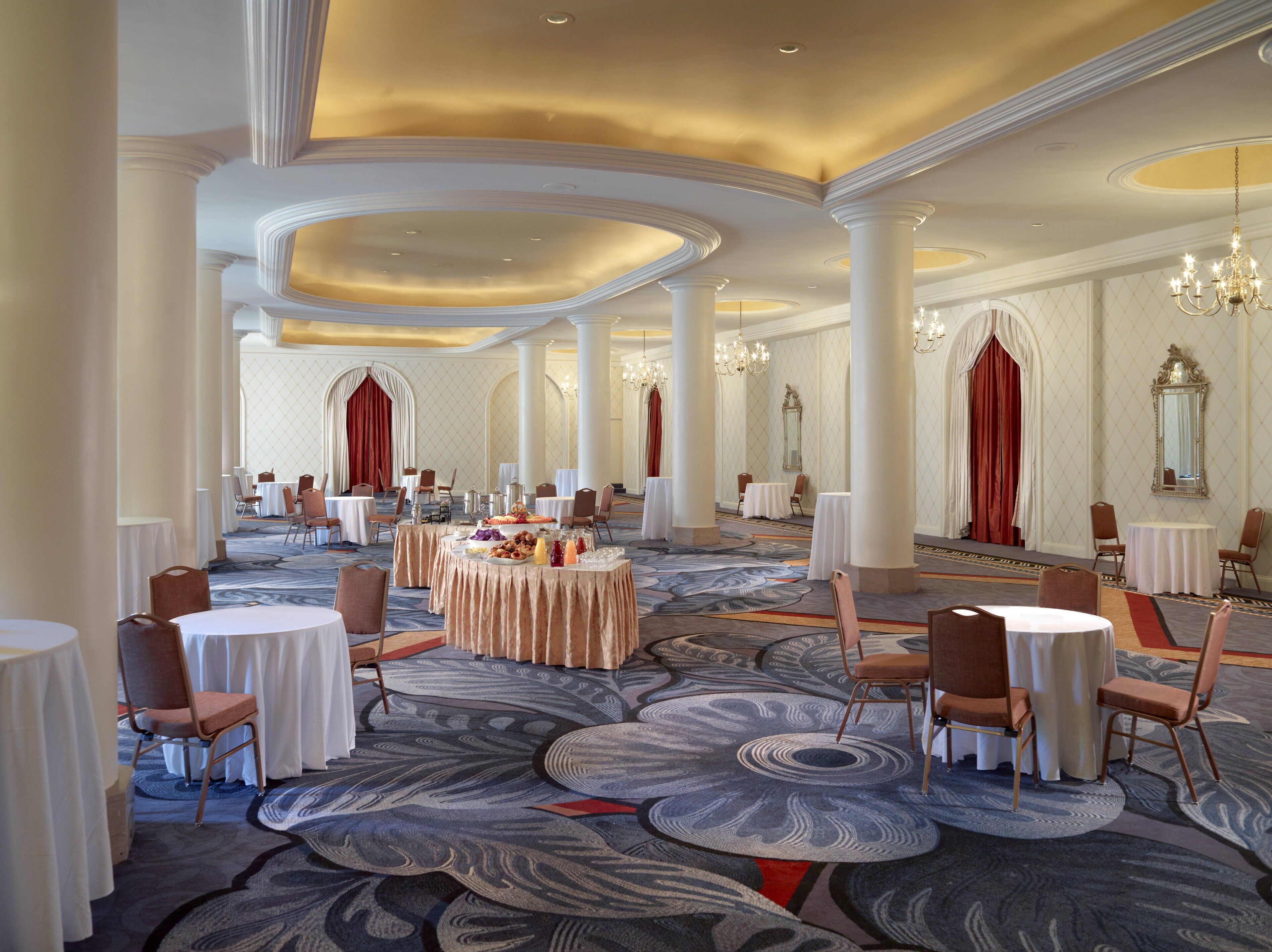 A spacious banquet hall with round tables, chairs, and a central buffet area.