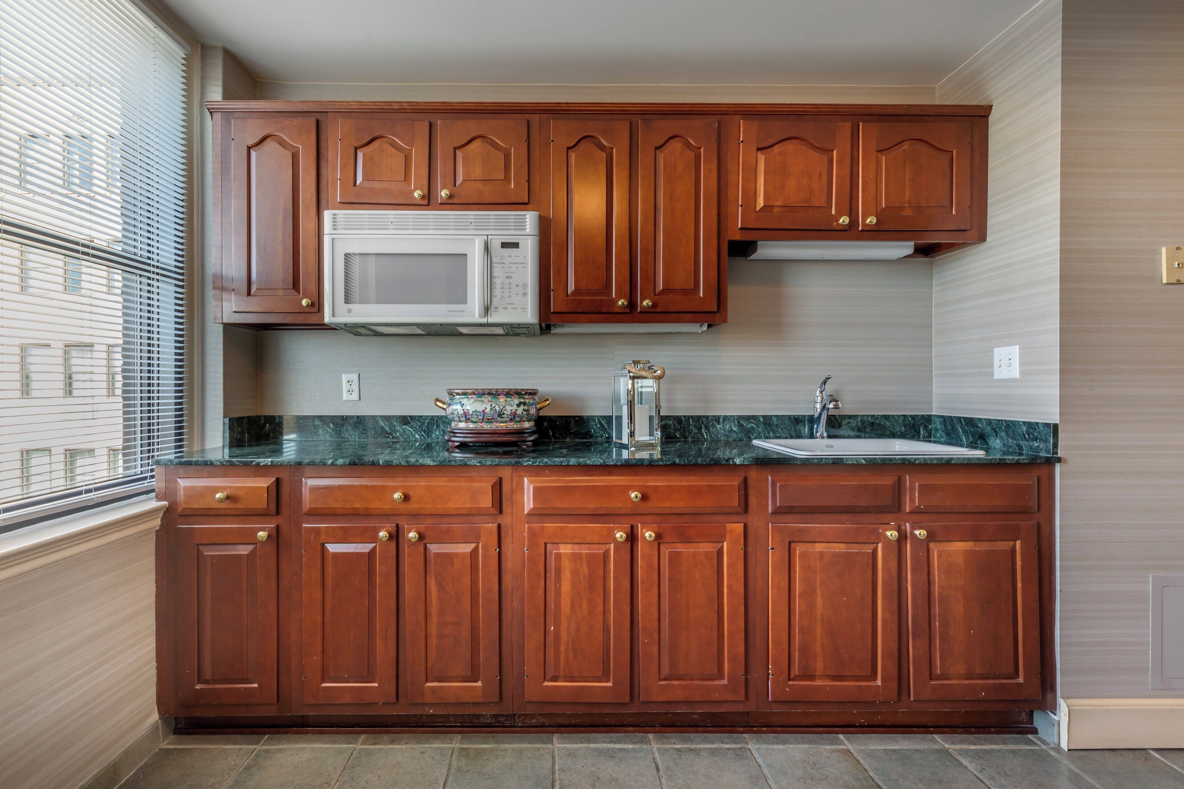A kitchen with wooden cabinets, a microwave, a sink, and a window with blinds.