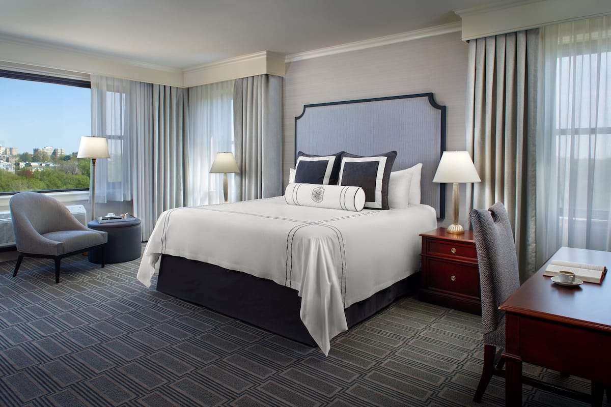 A hotel room with a large bed, two bedside tables, a desk, a chair, and a view of the city.