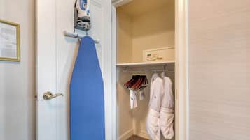 Una habitación con una puerta blanca, una tabla de planchar, un perchero con ropa y una bata colgada.