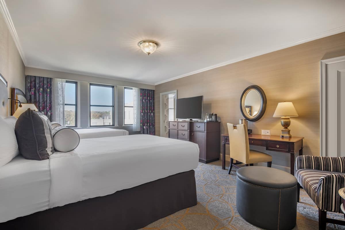 A hotel room with a large bed, a desk, a chair, a television, a mirror, and a window with curtains.