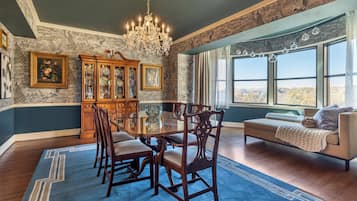 A dining room with a large table, chairs, a chandelier, and a view of the outdoors through large windows.