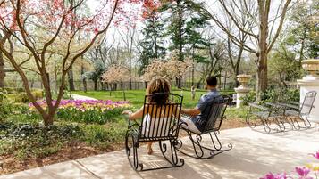 Relax in a serene garden setting with two comfortable rocking chairs and a beautifully manicured lawn.
