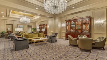 A spacious lobby with a patterned carpet, a large chandelier, and a classic wooden bookcase.