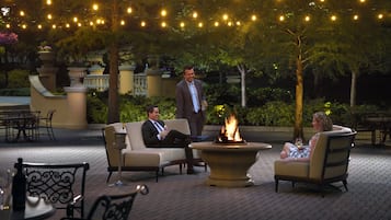 An outdoor seating area with a fire feature, surrounded by potted plants and string lights.