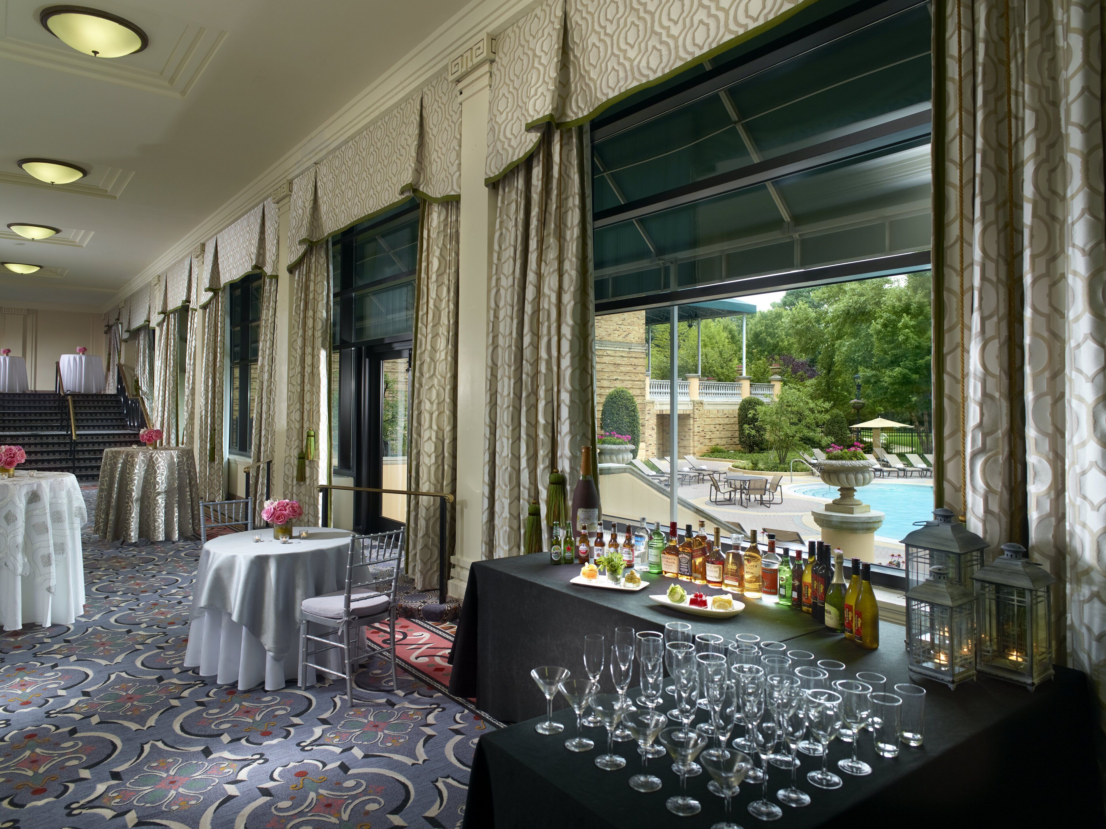 A hotel room with a large window, a table with bottles and glasses, and a carpeted floor.