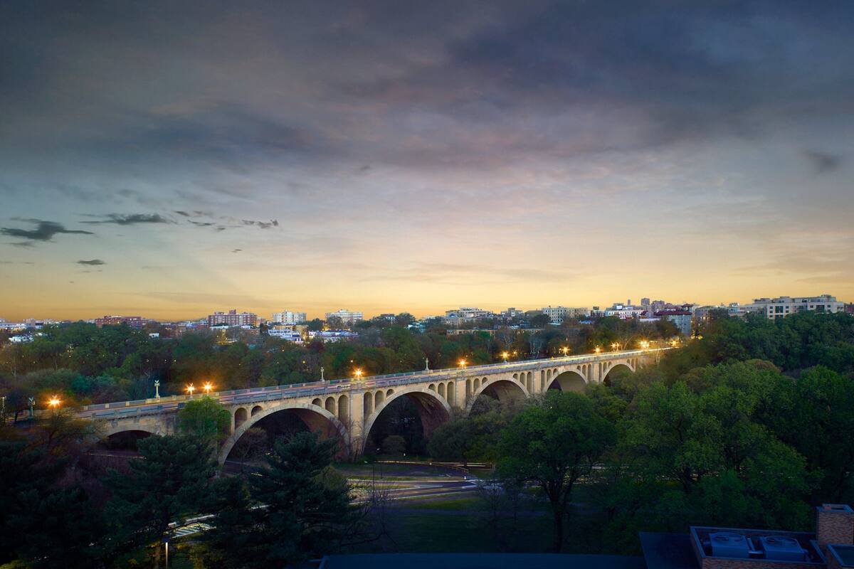 A bridge with multiple arches spanning over a body of water, surrounded by trees and buildings in the background.